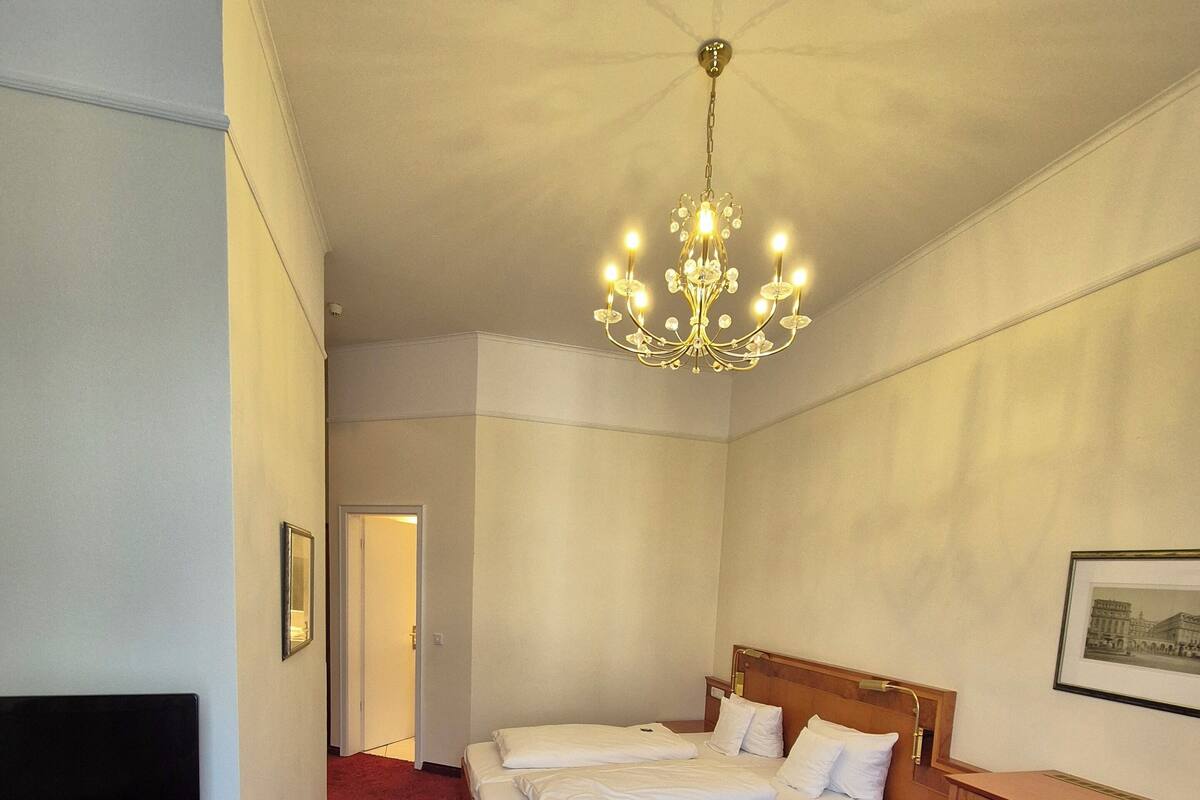 A hotel room with a large bed, a TV, a wooden nightstand, a desk, and a chandelier.