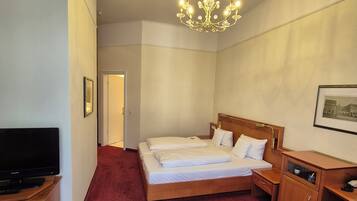A hotel room with a large bed, a TV, a wooden nightstand, a desk, and a chandelier.
