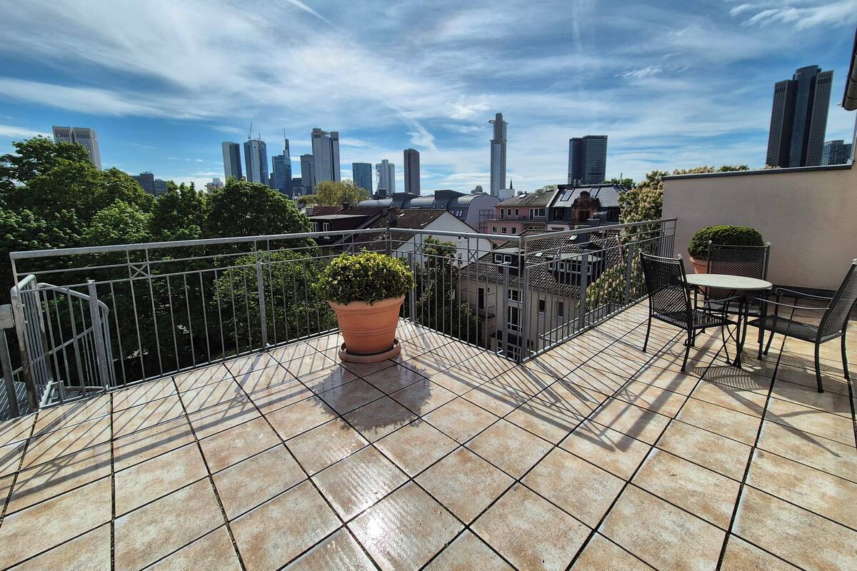 A rooftop terrace with a tiled floor, a potted plant, and a table with chairs.