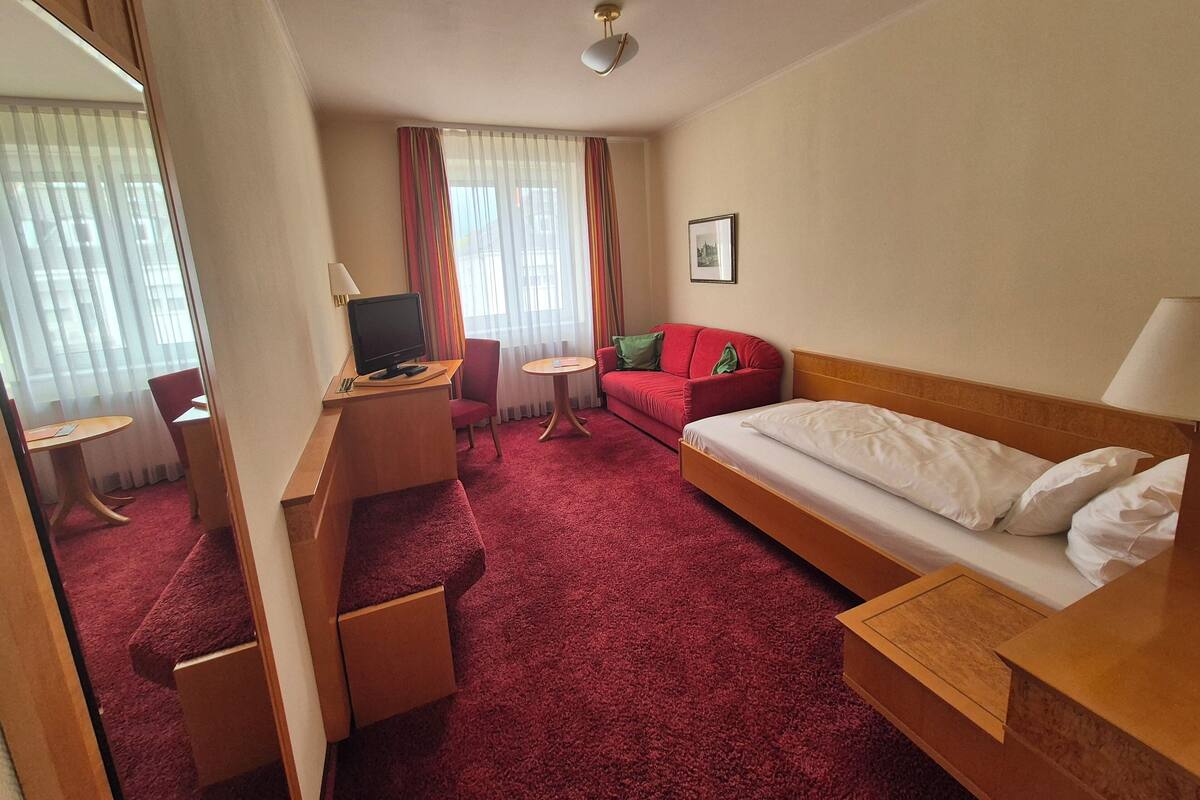 A hotel room with a bed, a desk with a computer, a red sofa, and a small round table.
