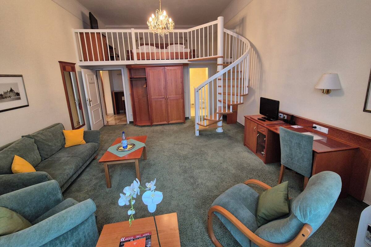 A living room with a sofa, armchair, coffee table, TV, and a staircase leading to an upper level.