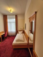 Habitación de hotel con una cama individual, escritorio, silla, espejo y ventana con cortinas.