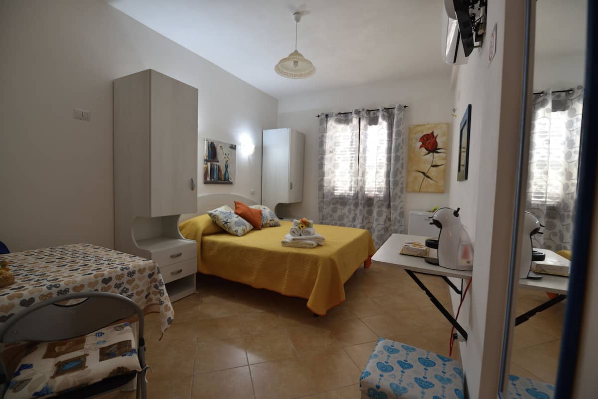 A bedroom with a bed, bedside table, wardrobe, and a small desk with a kettle.