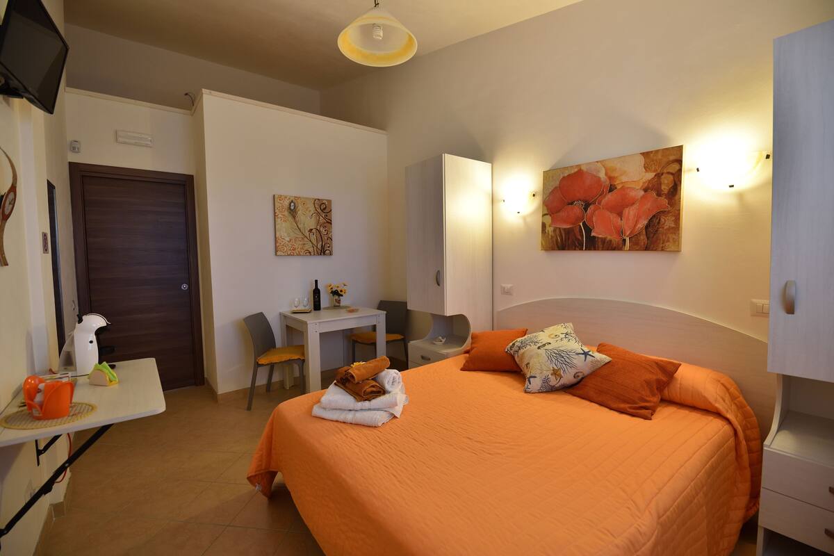 A hotel room with a bed, a desk, a chair, a table, and a door.
