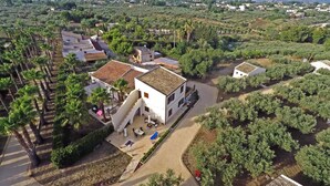 A white building with a tiled roof, surrounded by palm trees and a garden. - Agrisicilia (Castelvetrano)
