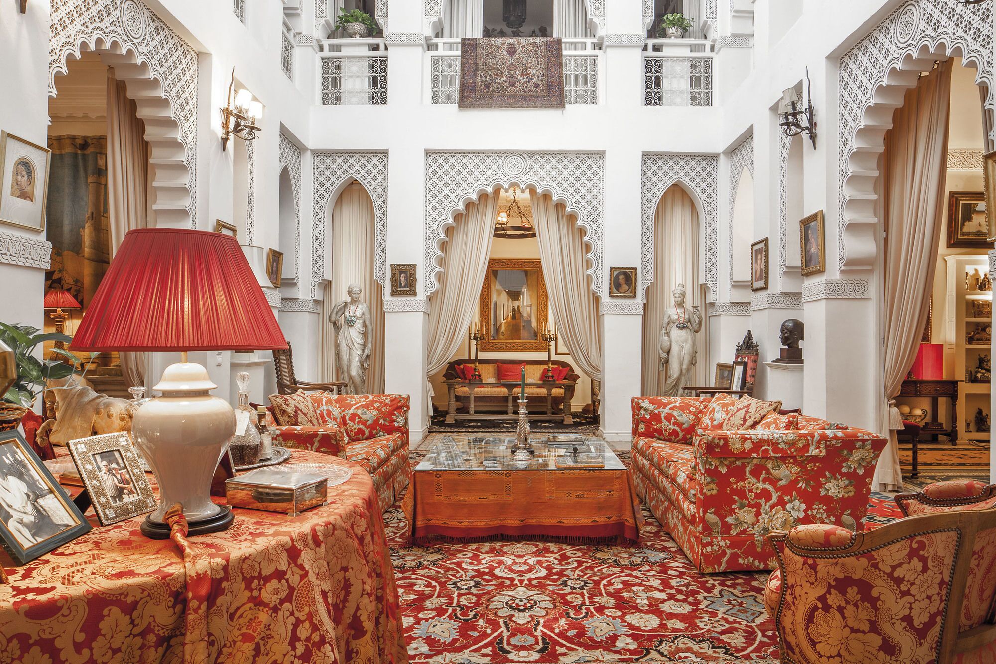 A traditional interior with ornate arches, a central seating area with a sofa and ottoman, and a red lamp.