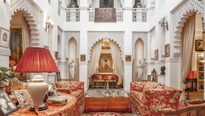 A traditional interior with ornate arches, a central seating area with a sofa and ottoman, and a red lamp. - Dar El Mudal - Adults Only (Marrakech)