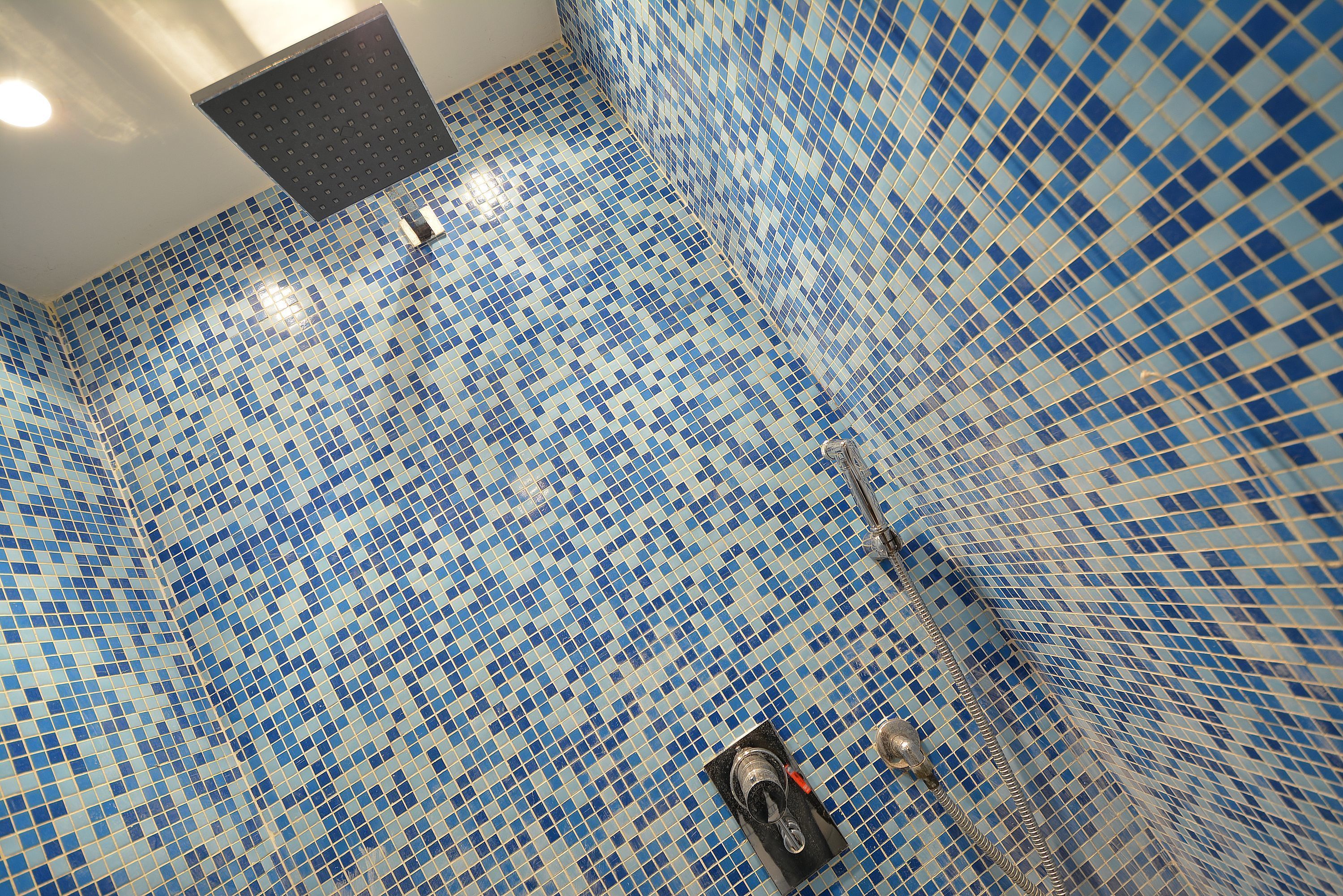 A bathroom with blue mosaic tile walls and a shower area.
