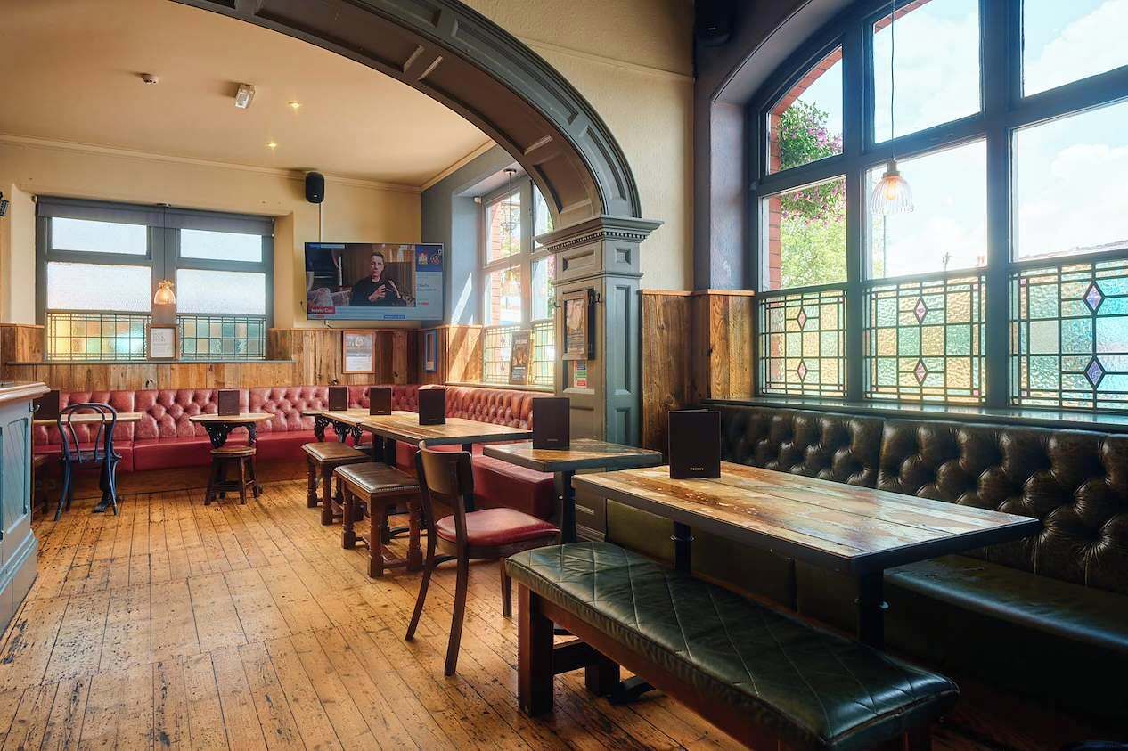 A restaurant interior with wooden flooring, leather booths, and tables.