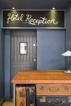 A hotel reception area with a sign reading "Hotel Reception" above a wooden counter. There are two suitcases on the counter. - The Wellington (Bristol)