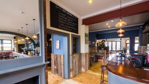 A bar area with a wooden floor, bar stools, and a chalkboard menu listing snacks. - The Wellington (Bristol)