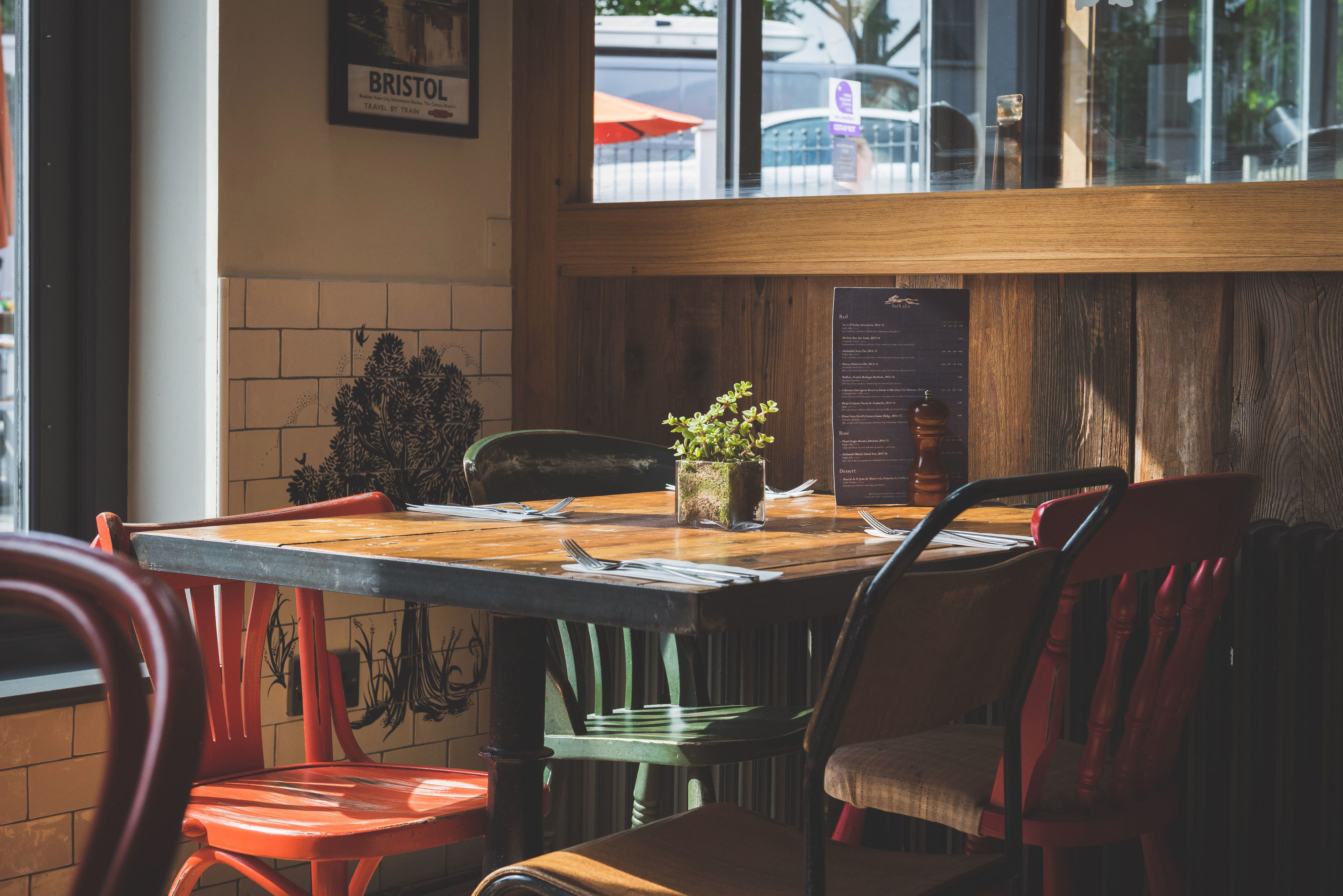Une table en bois sur laquelle est posée une plante en pot, entourée de chaises dont les sièges sont recouverts d’un tissu rouge et vert.