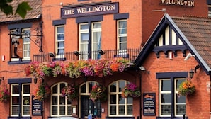 A traditional pub named "The Wellington" with a classic brick facade, large windows, and hanging flower baskets. - The Wellington (Bristol)