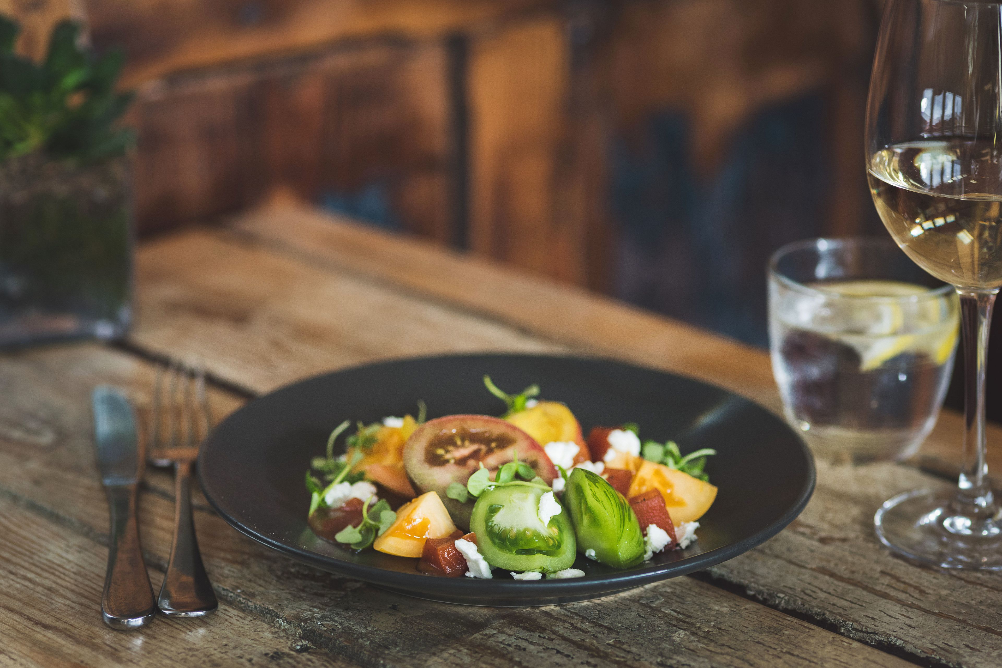A black plate with a salad on a wooden table.