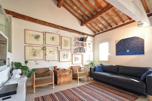 Una sala de estar con techo de madera, un sofá, una mesa de centro, una estantería y cuadros enmarcados en la pared.