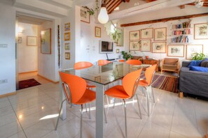 Una sala de estar moderna con una mesa de comedor de vidrio, sillas color naranja, un sofá y una estantería.