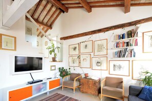 Una sala de estar con televisor, muebles naranja y blanco, vigas de madera y obras de arte enmarcadas en las paredes.