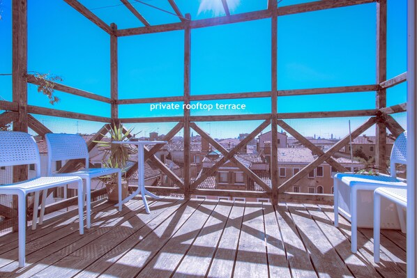 Una terraza privada en la azotea con suelo de madera, sillas blancas y vistas a la ciudad.