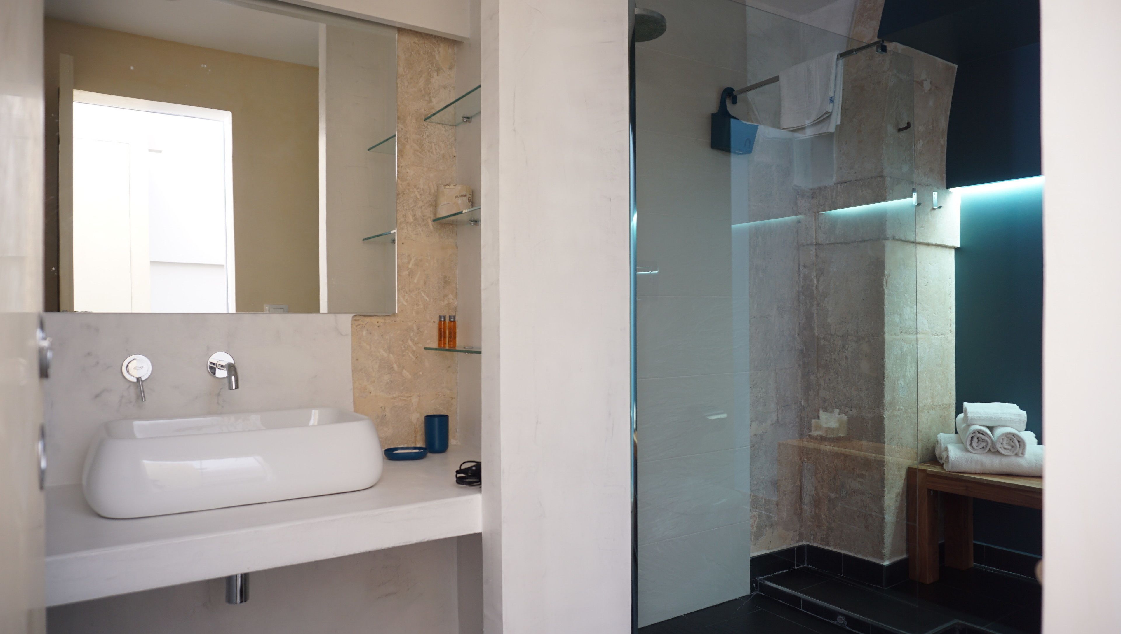 Un baño moderno con un espejo grande, un lavamanos blanco y una zona de ducha con paredes de vidrio.