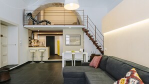 A modern living space with a grey sofa, a colorful pillow, a staircase, a dining area, and a kitchen. - 1743 Loft Siracusa (Syracuse)