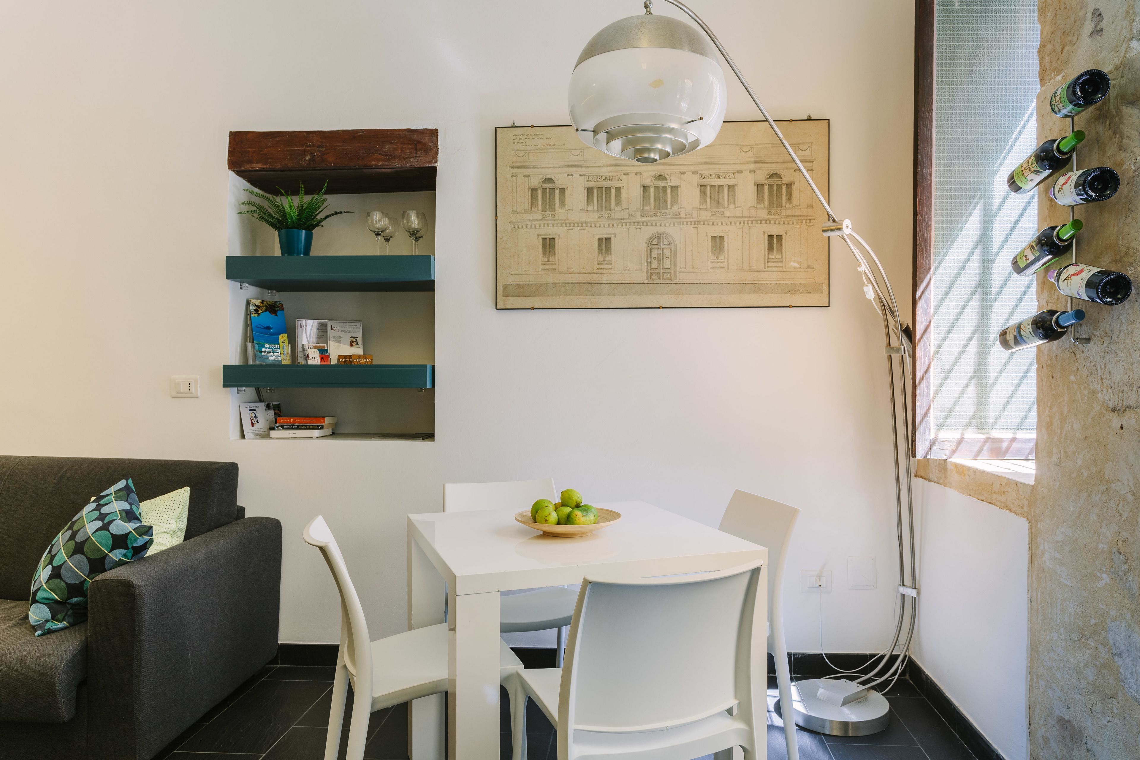 A modern living space with a dining area, a sofa, a white table, and a wall-mounted wine rack.