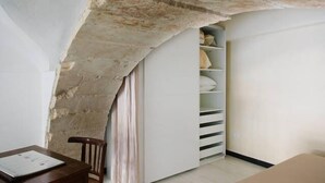 A room with a stone wall, a wooden chair, a desk with papers, and a white wardrobe with shelves. - 1743 Loft Siracusa (Syracuse)