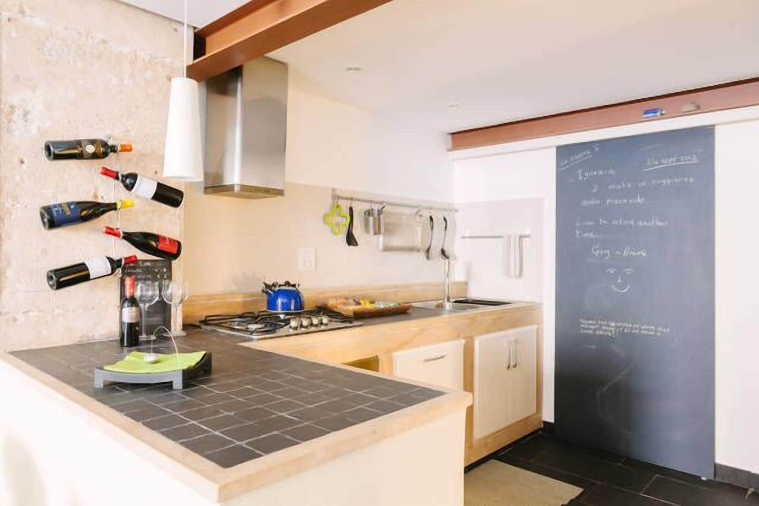 A modern kitchen with a central island, a chalkboard with writing, and wine bottles on the wall.