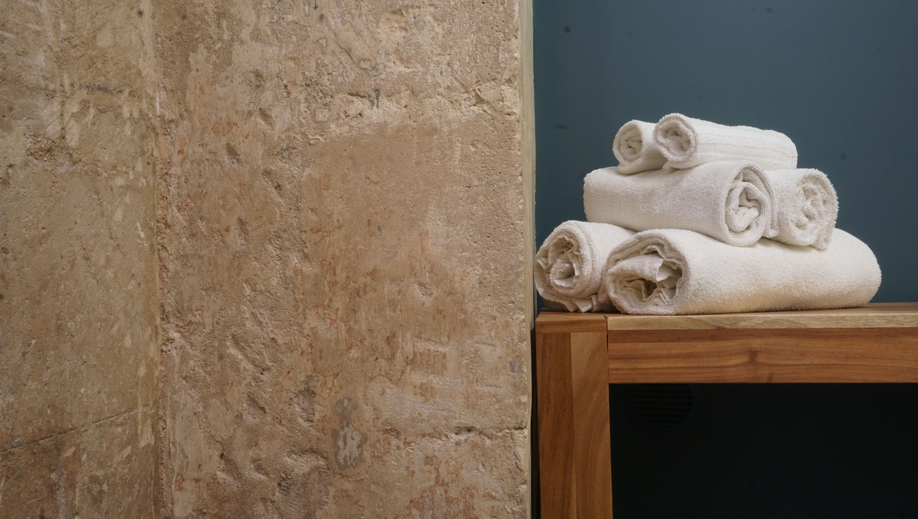 A stack of white towels on a wooden table against a textured beige wall.