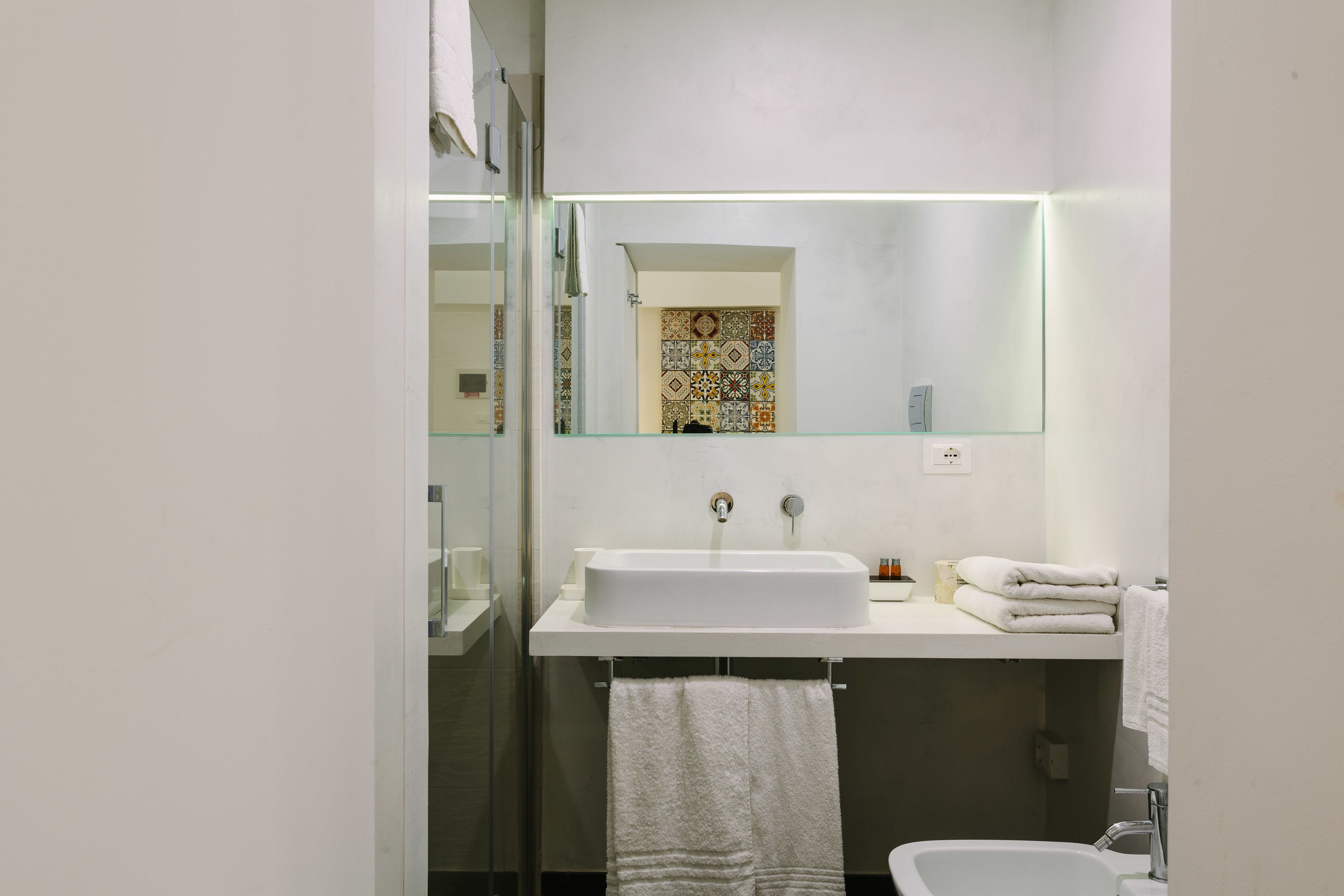 Ein modernes Badezimmer mit einem weißen Waschbecken, einer Duschkabine aus Glas und einer gefliesten Rückwand.