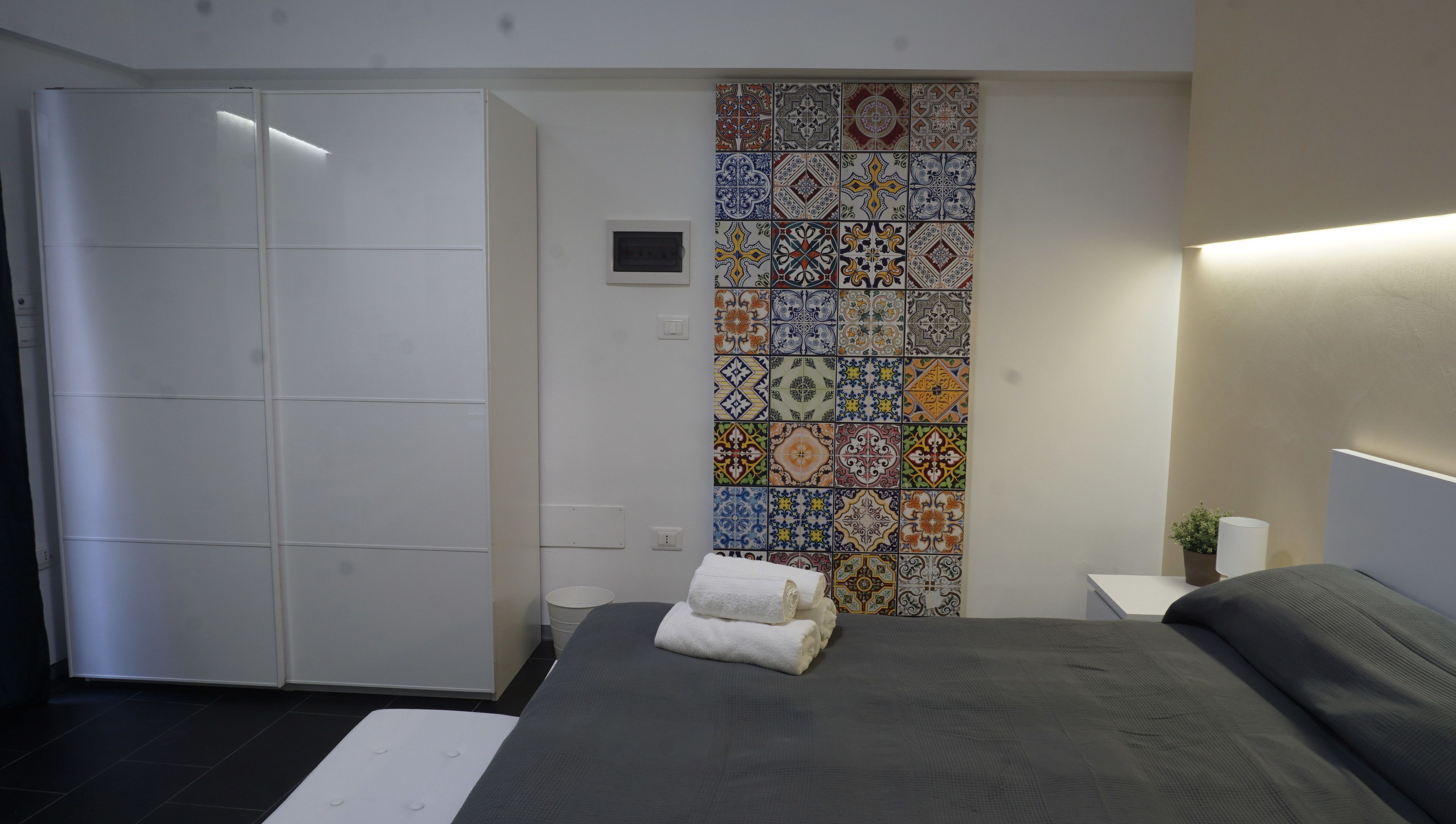 A modern bedroom with a large bed, a wardrobe, and a decorative tile wall.