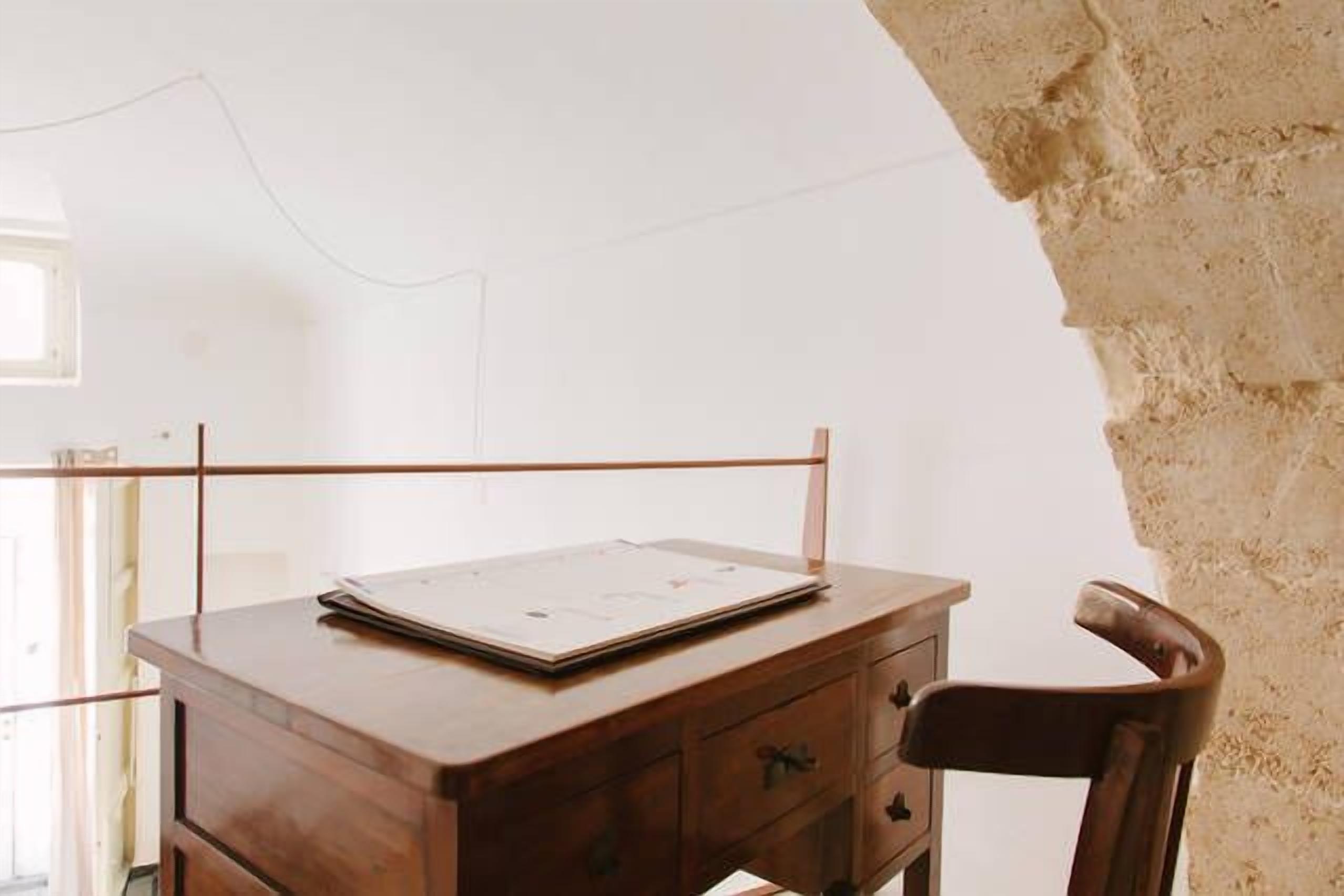 Uma mesa de madeira com um laptop e papéis, uma cadeira e uma parede de pedra.