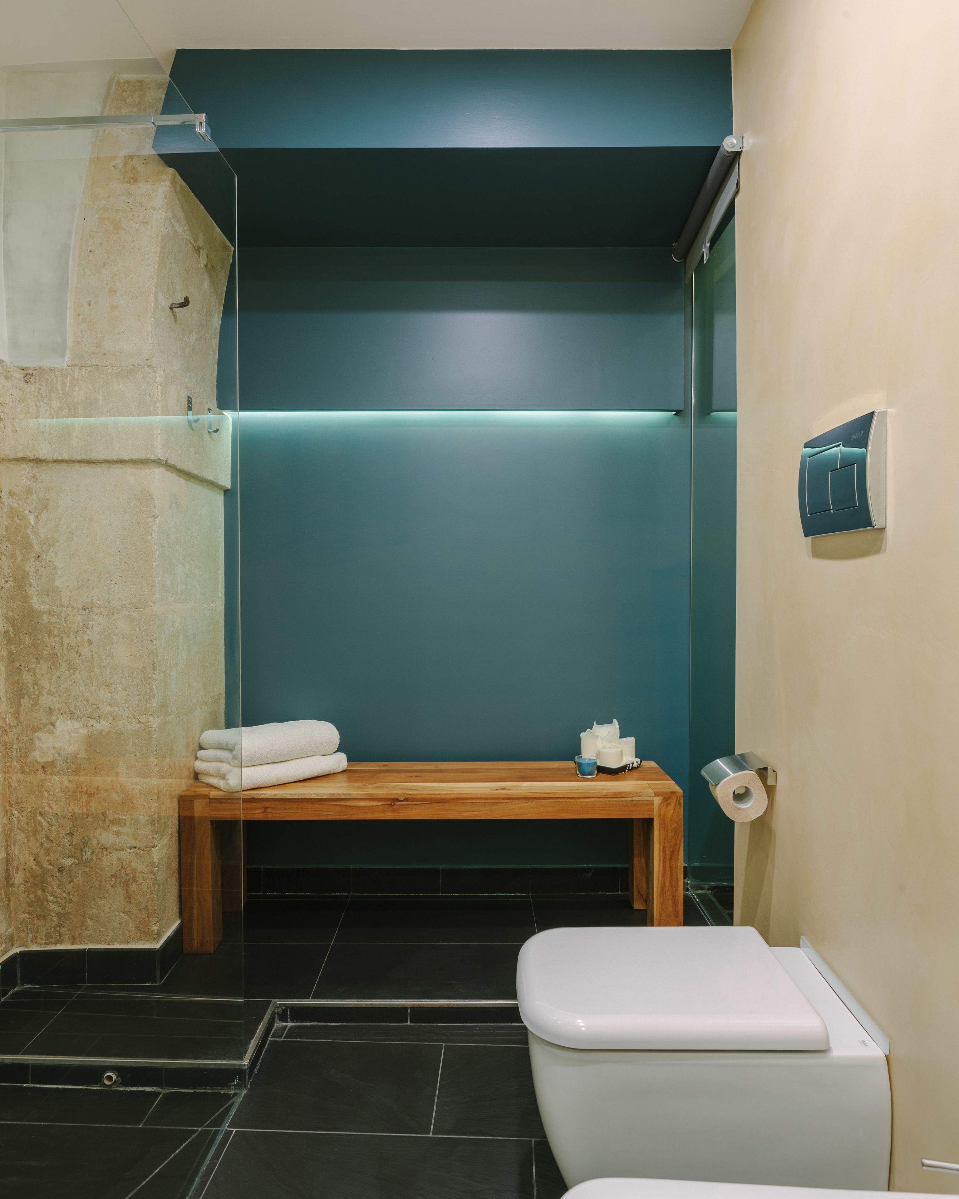 Un baño moderno con un banco de madera, un inodoro y un perchero para toallas.