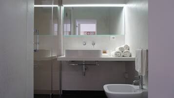 Un baño moderno con cabina de ducha de vidrio, un lavamanos blanco, un bidé y un perchero para toallas.