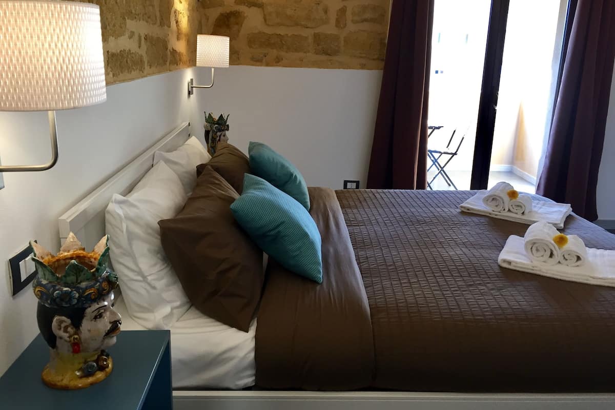 Habitación de hotel con cama, mesita de noche, lámpara, un florero decorativo y vistas al exterior.