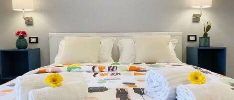 A hotel room with a neatly made bed, two bedside lamps, a vase with flowers, and a cactus on the nightstand.