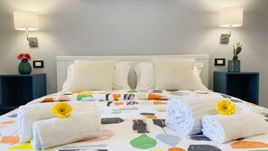 A hotel room with a neatly made bed, two bedside lamps, a vase with flowers, and a cactus on the nightstand. - B&B Donna Teresa (Agrigento)