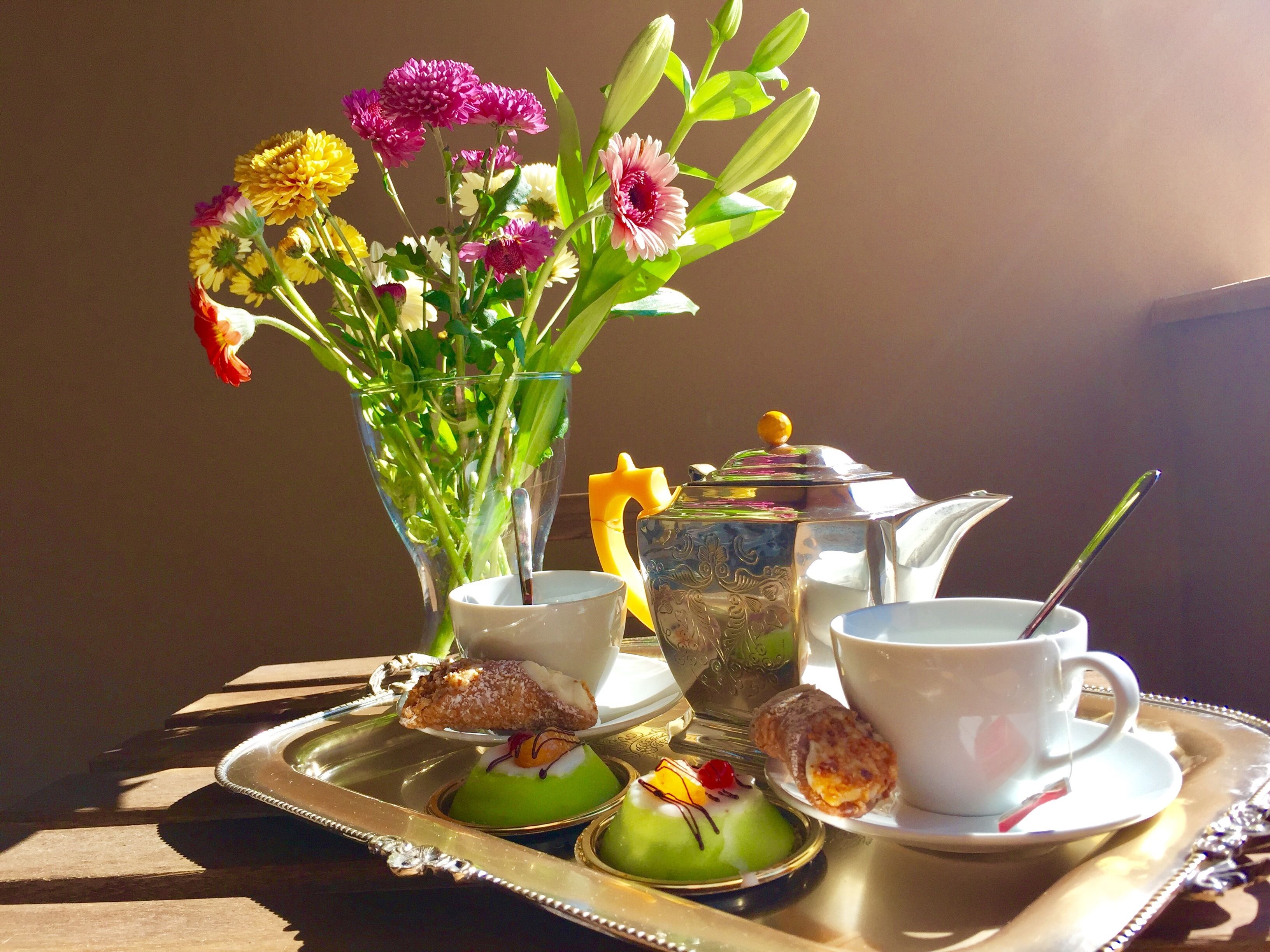Un plateau avec une théière, des tasses et des pâtisseries, accompagné d’un vase de fleurs.