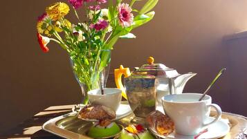 Una bandeja con tetera, tazas y pasteles, junto a un jarrón de flores.