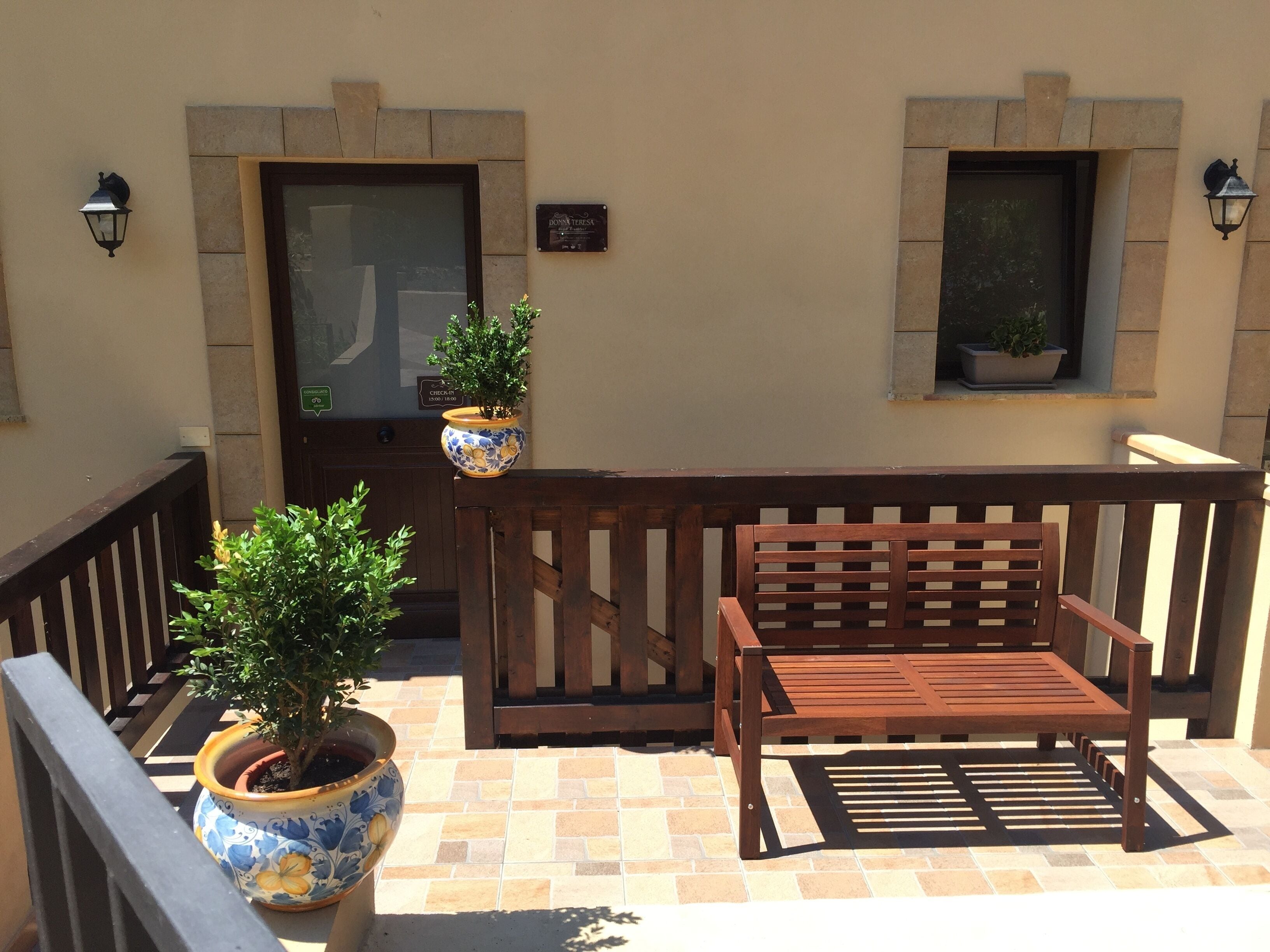 A wooden bench and two potted plants on a tiled patio.