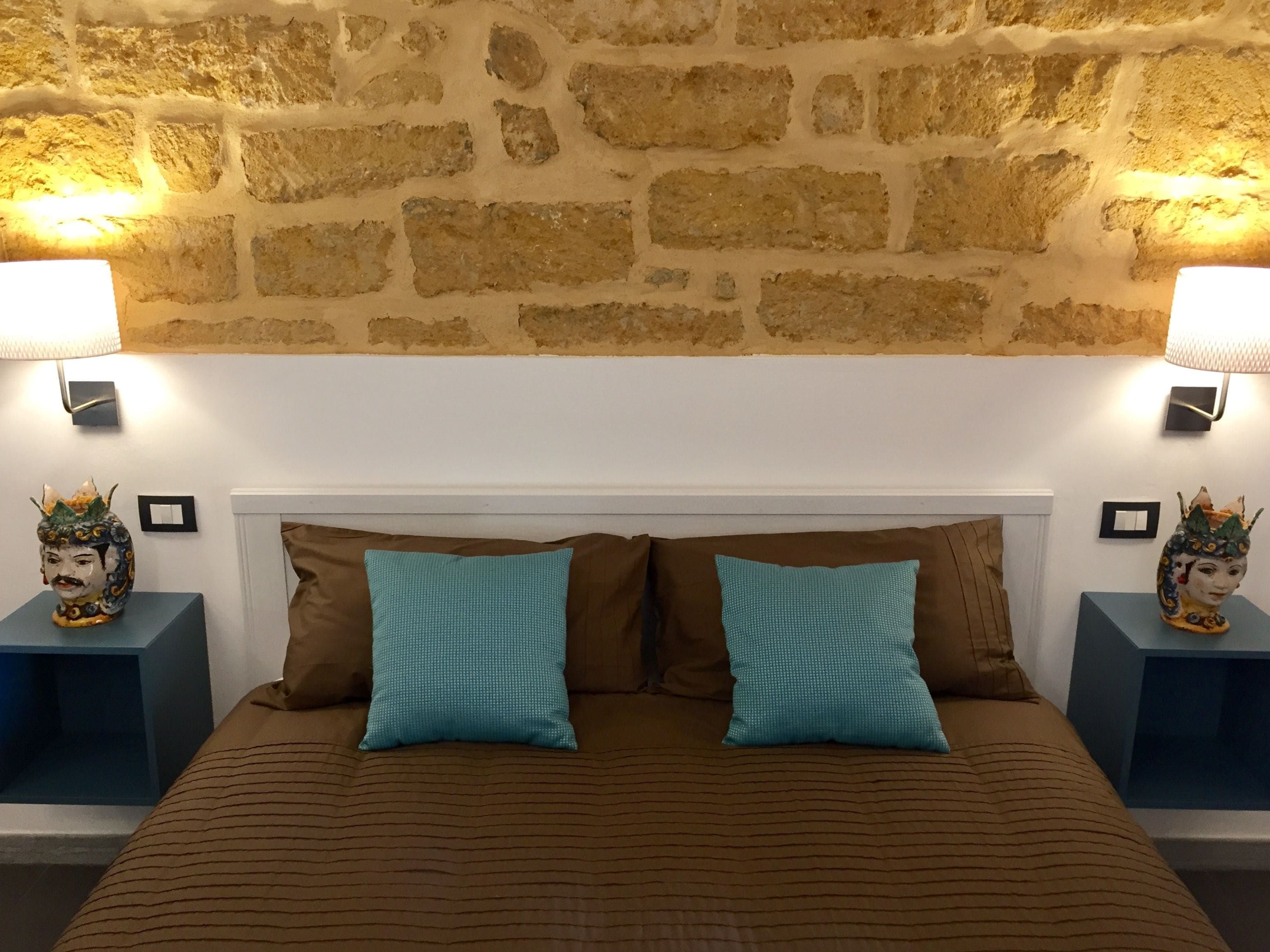 Ein Bett mit einer braun gestreiften Tagesdecke, zwei türkisfarbenen Kissen und zwei Nachttischen mit Dekoration und Wandleuchten.