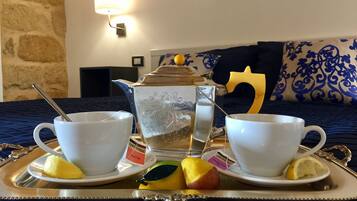 A breakfast tray with two white cups, a teapot, and fruit on a bed with a blue bedspread.