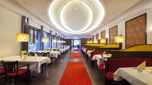 A hotel corridor with tables and booths, a red carpet, and decorative wall panels. - Eilenriedestift Hotel (Hannover)