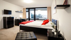 A modern hotel room with a large bed, a desk, a chair, a TV, and a window with a view. - Eilenriedestift Hotel (Hannover)