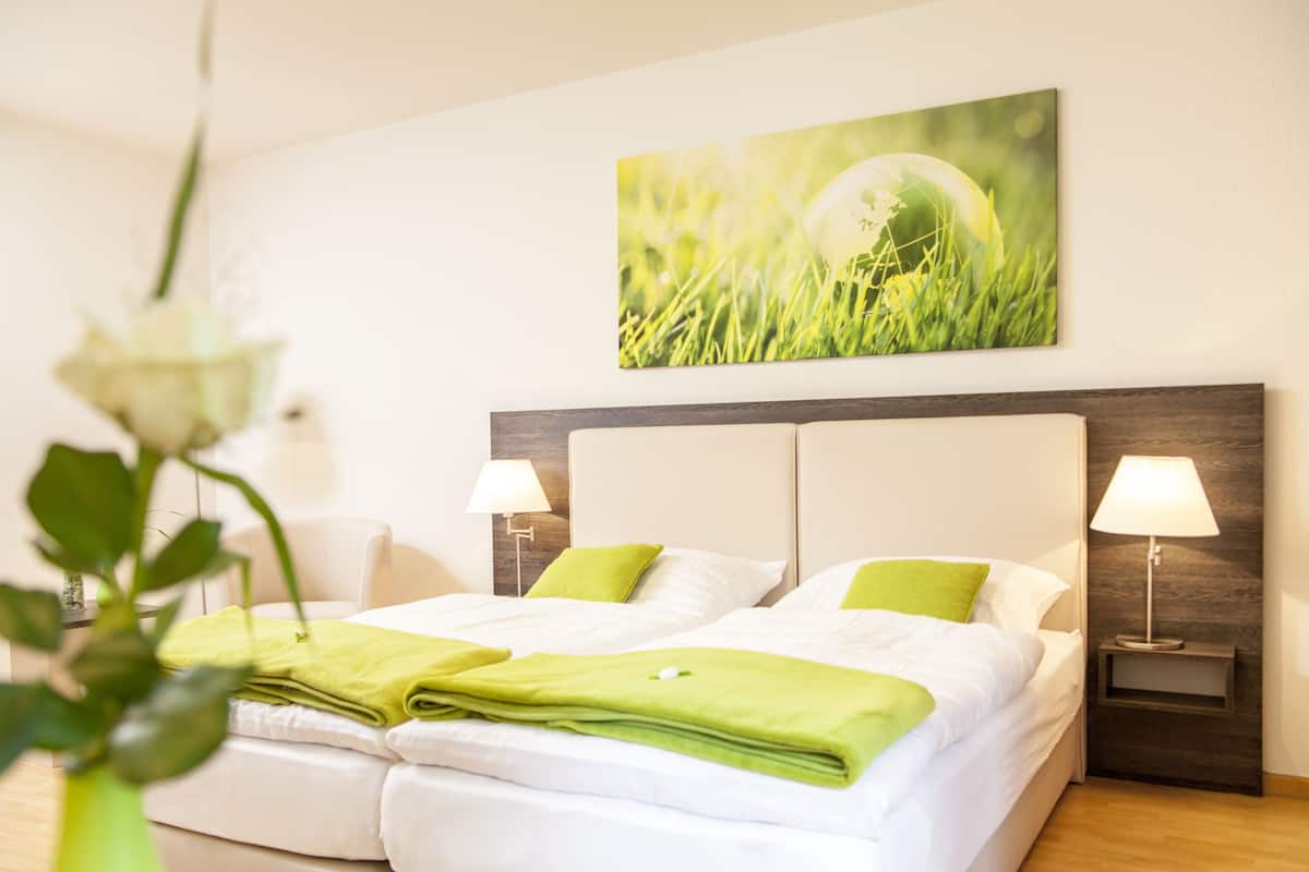 A hotel room with a neatly made bed, two bedside lamps, and a wall-mounted painting of grass.