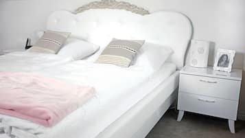 Una cama bien hecha con cabecera blanca, dos almohadas, una mesita de noche con una foto enmarco y un cajón.