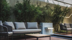 A modern outdoor seating area with a sofa, chairs, and a table, surrounded by lush greenery. - Eilenriedestift Hotel (Hannover)