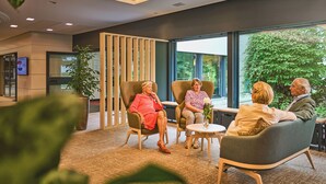 A group of people seated in a modern lounge area with large windows and indoor plants. - Eilenriedestift Hotel (Hannover)