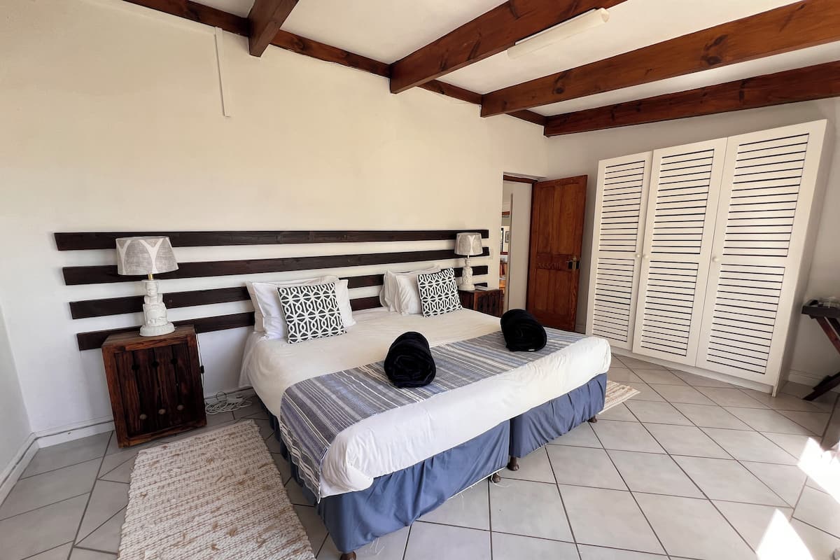 Een slaapkamer met een bed, nachtkastjes, een houten hoofdbord, een raam met luiken en een betegelde vloer.