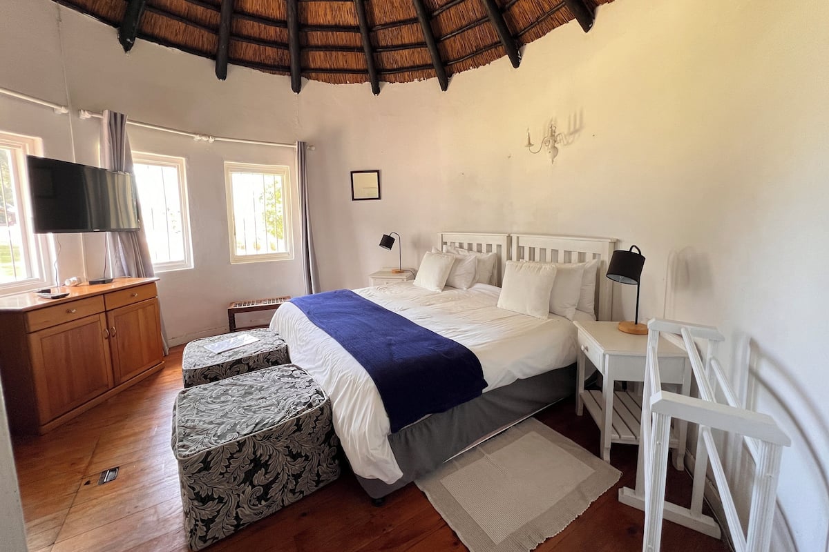 Een slaapkamer met een bed, nachtkastjes, een bureau, een televisie en een raam.