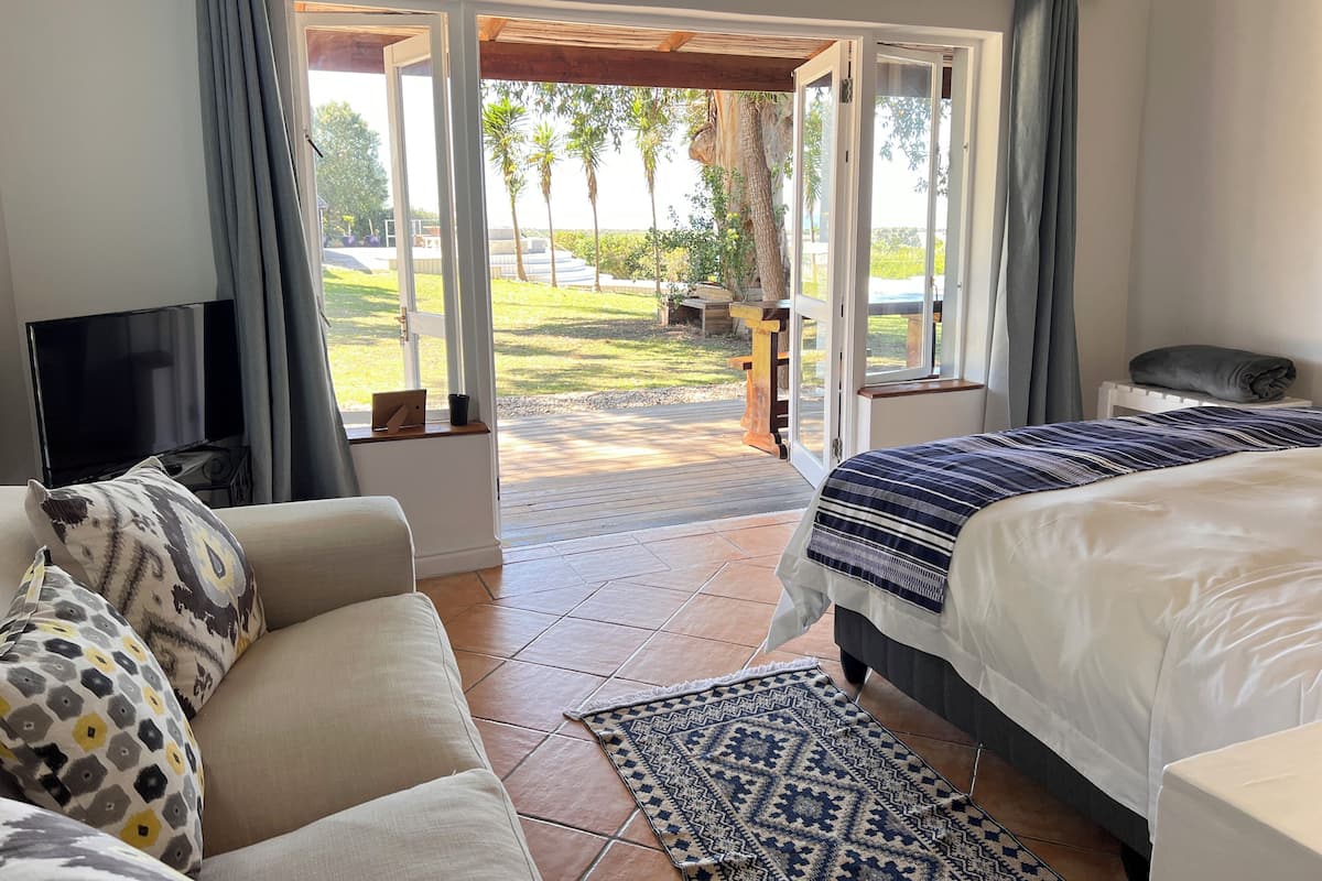Een slaapkamer met een slaapbank, een bed, een televisie en uitzicht op een tuin via openslaande deuren.